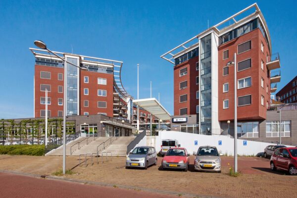 Vooraanzicht van het Harriet Freezerhof, een modern wooncomplex met rode bakstenen gevels en parkeergelegenheid.